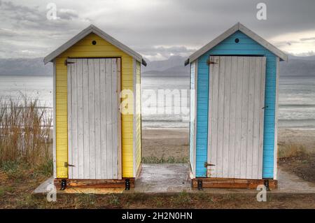 Due piccole case portabili blu e giallo sulla spiaggia in una giornata buia e arida Foto Stock