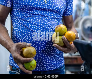 Uomo che indossa una camicia blu con piccoli dettagli che tiene i limoni in entrambe le mani. Fiera di Sao Joaquim, Salvador, Bahia, Brasile. Foto Stock