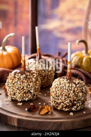 Mele al caramello ricoperte di noci su un piatto di legno con sfondo autunnale da una finestra Foto Stock