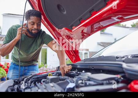 Uomo che guarda il motore dopo l'auto guasto chiamata recupero automatico sul telefono cellulare Foto Stock