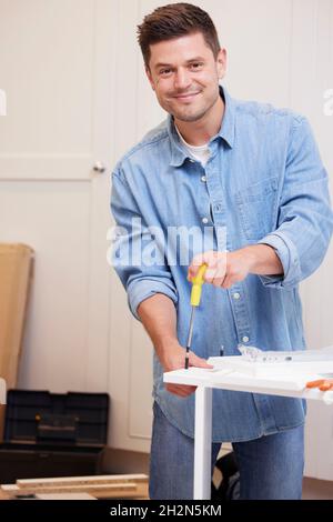 Ritratto di uomo che mette insieme il mobile di auto-assemblaggio a casa Foto Stock