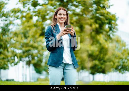 Freelance femminile che parla sugli smartphone mentre si appoggia alla parete Foto Stock