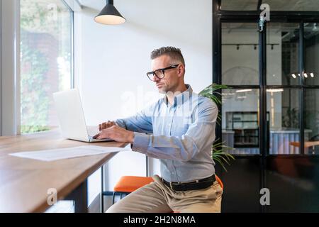 Uomo d'affari che utilizza il computer portatile mentre si siede alla scrivania Foto Stock