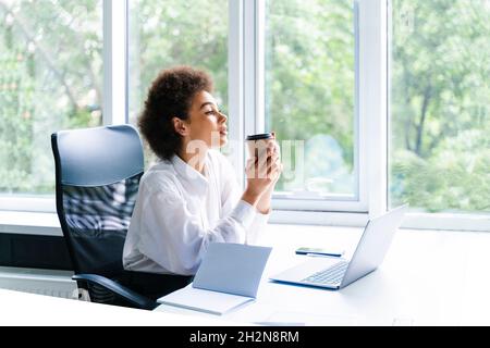 Giovane donna professionista che ha un caffè alla scrivania in ufficio Foto Stock