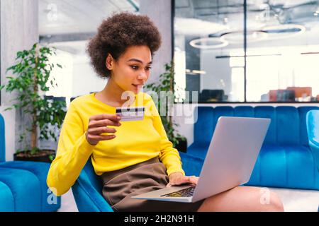 Donna d'affari che tiene la carta di credito mentre usa il laptop nella lobby dell'ufficio Foto Stock
