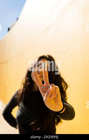 Donna gesturante segno di pace di fronte al muro Foto Stock