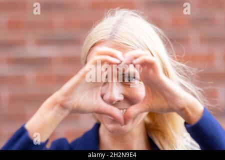Donna matura che fa il simbolo del cuore con le mani Foto Stock