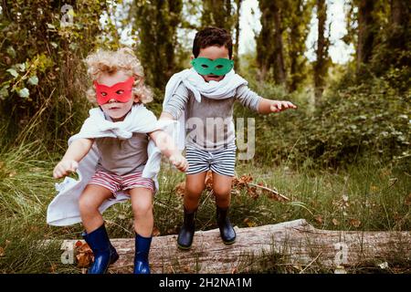 I ragazzi giocosi indossano maschere e cappe che saltano insieme nella foresta Foto Stock