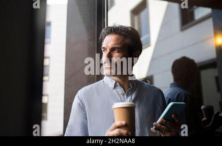 Professionista di sesso maschile che parla sul telefono cellulare mentre si ha un caffè in camera Foto Stock