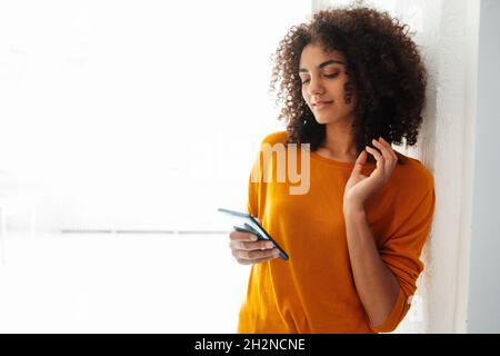 Afro giovane donna messaggi di testo tramite smartphone a casa Foto Stock