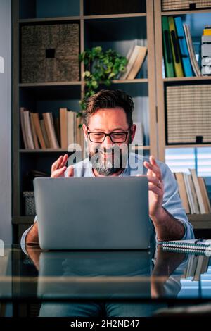 Sorridente freelance maschile che si muove durante le videochiamate sul laptop mentre lavora a casa Foto Stock