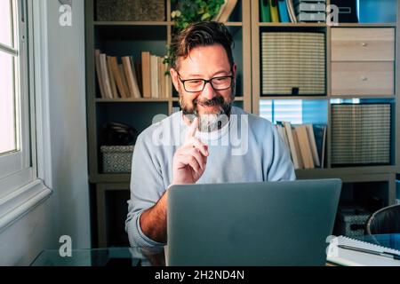 Un uomo d'affari sorridente che si sta gestendo durante le videochiamate sul laptop mentre lavora a casa Foto Stock