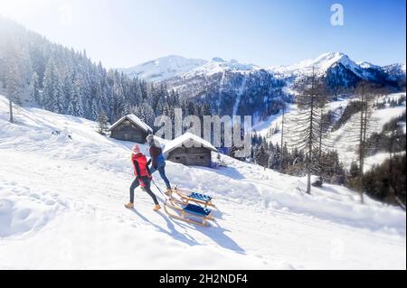 Donna sorridente slittante con l'uomo sulla neve durante l'inverno Foto Stock