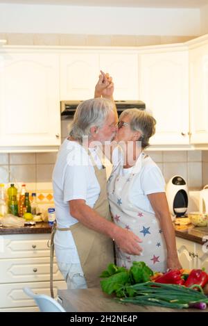 Coppia anziana che tiene le mani mentre bacia in cucina Foto Stock