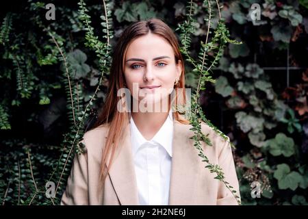 Giovane professionista femminile con capelli biondi in piedi da piante Foto Stock