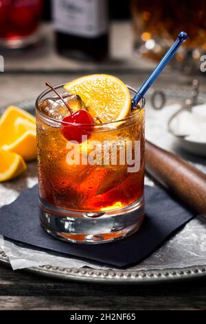 Cocktail vecchio stile in Rocks Glass con ingredienti e utensili da bar nel Dark Vintage Wooden Bar Foto Stock