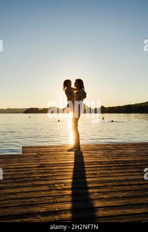 Madre che porta la figlia mentre si trova sul molo durante il tramonto Foto Stock