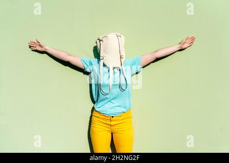 Donna che ricopre il viso con zaino in piedi davanti al muro verde durante la giornata di sole Foto Stock