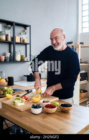 Uomo anziano sorridente che stringe il limone sulla centrifuga al banco della cucina Foto Stock