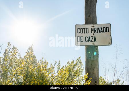 Primo piano di un cartello in metallo della riserva di caccia privata su un palo di legno, scritto in lingua spagnola. Campo rurale pieno di Genista al tramonto Foto Stock