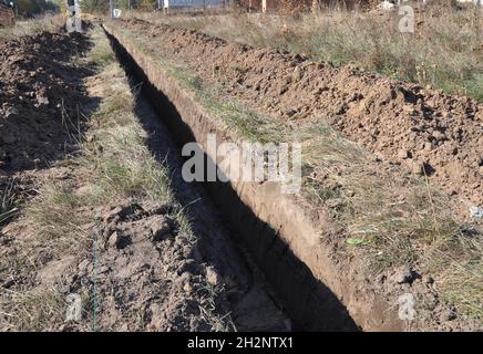 Lavori di terra, scavo trincea. Trincea di terra lunga scavata per posare tubo o fibra ottica. Scavando una trincea. Foto Stock