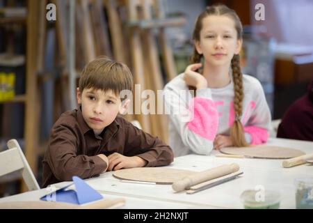 Una ragazza ed un ragazzo sono seduti ad una scrivania in una lezione di modellazione di argilla. Foto Stock