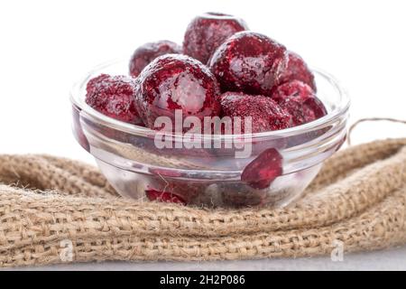 Diverse ciliegie rosse surgelate dolci e organiche snocciolate in un piatto di vetro su un burlap, primo piano, isolate su bianco. Foto Stock