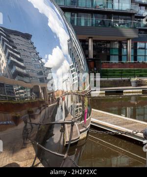 Un approccio riflessivo - scultura di un ragazzo che spinge una sfera riflettente al Clarence Dock, nel centro di Leeds Foto Stock