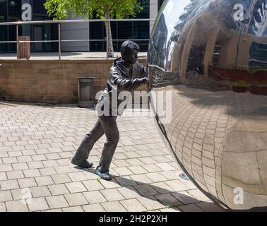 Un approccio riflessivo - scultura di un ragazzo che spinge una sfera riflettente al Clarence Dock, nel centro di Leeds Foto Stock