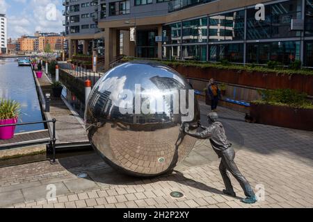 Un approccio riflessivo - scultura di un ragazzo che spinge una sfera riflettente al Clarence Dock, nel centro di Leeds Foto Stock