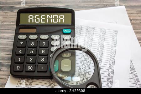 Su un tavolo di legno, i numeri su carta e una calcolatrice con il testo Agenda Foto Stock