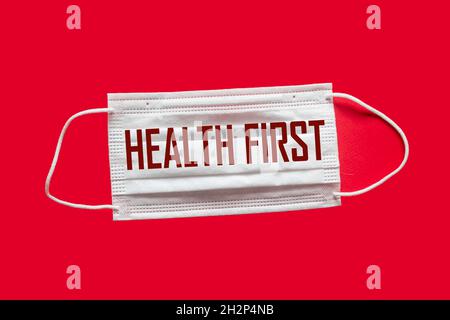 Maschera medica con il testo prima Salute, su sfondo rosso. Giornata mondiale della salute. Concetto di assistenza sanitaria. Posiziona per testo. Messa a fuoco soft. Vista dall'alto. Foto Stock