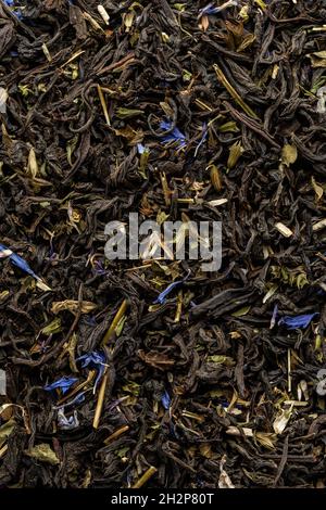 Mucchio di foglie di tè secco. Tè nero secco. Sfondo testurizzato di foglie secche di tè nero aromatico con fiori blu. Foto Stock