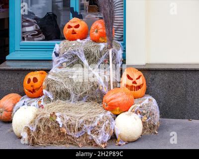 Zucche arancioni con facce divertenti scolpite su pagliacci e un broomstick sono un fumetto Halloween installazione vicino l'ingresso di un edificio residenziale. Foto Stock