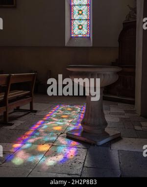 La luce del sole diffonde l'immagine multicolore della vetrata a St-Pierre Eglise, Cabrerets, Lot Valley Francia Foto Stock