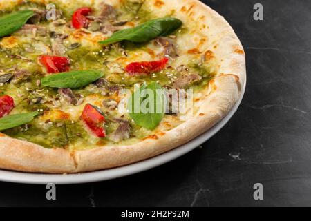 Deliziosa pizza calda fatta in casa su un tavolo di marmo nero. Pizza - pizza fatta in casa con carne, formaggio, salsa di pomodoro, pomodori, semi di zucca e basilico. Foto Stock