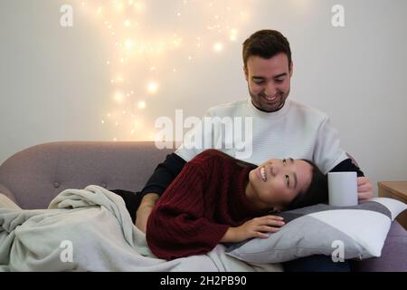 Giovane coppia allegra multirazziale che si guarda l'un l'altro e sorride sul divano. Foto Stock