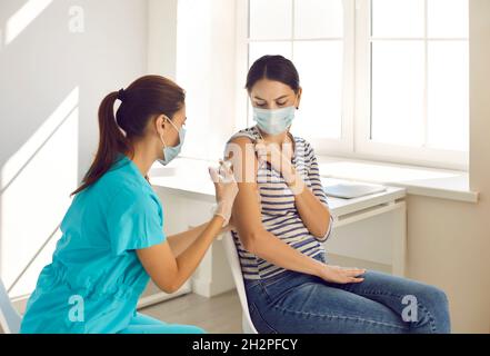 Donna in maschera medica viso riceve la dose di vaccino di immunizzazione coronavirus da infermiere. Foto Stock