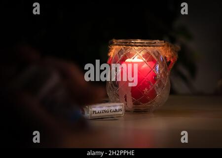 primo piano di carte da gioco accanto a una candela rossa in un bicchiere su un tavolo di notte. sfondo scuro e sfocato Foto Stock