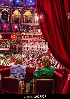 ALBERT HALL INTERNO BBC Proms prestazioni con colleghe in primo piano la visione di musica le prestazioni utilizzando occhiali opera insediato nel lusso in velluto rosso casella privato con platea e palco orchestra palco in background Foto Stock