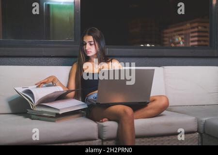 Giovane donna caucasica studio notturno sul divano della terrazza. Madrid, Spagna. Foto Stock