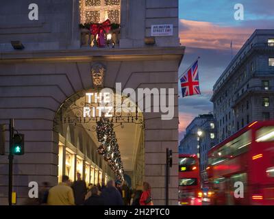 IL RITZ LONDON CHRISTMAS FOLLE il Ritz Hotel durante l'inverno affollata stagione festiva, luci notturne con il cartello "The Ritz" illuminato, con la bandiera di Union Jack, gli acquirenti e passando gli autobus rossi di Londra sfocati Arlington Street Piccadilly London UK Foto Stock