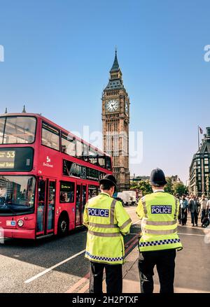 London Metropolitan Police ufficiali che indossano caschi e giubbotti ad alta visibilità sul Westminster Bridge Street Security duty back view con autobus rosso di londra al Westminster Bridge Houses of Parliament Londra UK Foto Stock