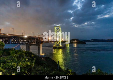 Le luci del ponte sospeso si mescolano con il bagliore del tramonto e le spettacolari nuvole Foto Stock