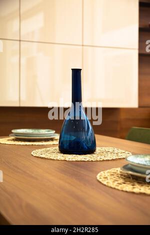 Moderna cucina interna, tavolo da pranzo in legno noce e bottiglia blu decorativa Foto Stock