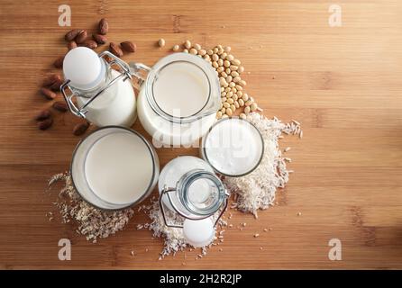 Varianti di latte vegano alternative a base di cereali e noci in bicchieri e bottiglie con ingredienti su un tavolo di legno, spazio copia, vie ad alto angolo Foto Stock