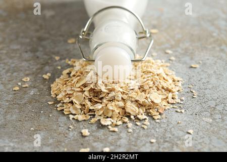 Latte di avena vegano, bottiglia con tappo si trova su un mucchio di farina d'avena su uno sfondo di pietra grigia, prodotto caseario alternativo, primo piano, spazio copia, selezionato Foto Stock