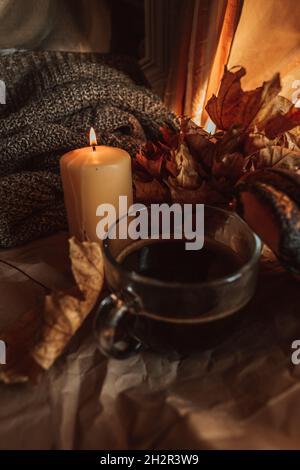 Candela che brucia e una tazza grande di caffè nero caldo in una casa accogliente autunno sera ancora vita con foglie secche. Foto Stock