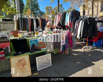 Mercato delle pulci stalla con vestiti di seconda mano. Al centro c'è una signora anziana seduta e in attesa di clienti. Foto Stock