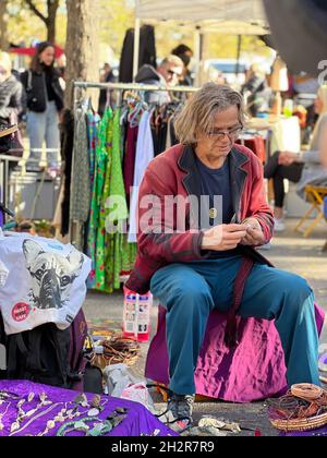 Uomo con occhiali che prepara la merce per la vendita presso uno stand del venditore in un mercato delle pulci a Zurigo. Dietro di lui c'è un trambusto di mercato delle pulci. Foto Stock